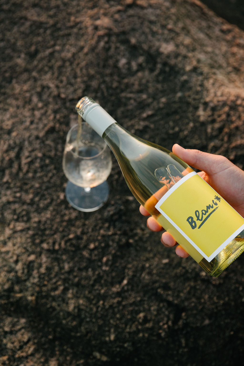 Hand holding a bottle of Blind Corner Organic Margaret River wine with a yellow label on a textured surface