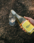 Hand holding a bottle of Blind Corner Organic Margaret River wine with a yellow label on a textured surface