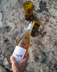 Hand pouring a bottle of Blind Corner's organic pinot grigio wine into an empty glass on a stony surface