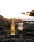 Bottle of Orange* in Colour Margaret River Organic wine being poured into a glass on a rocky surface with a scenic background.