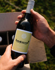 Person holding a bottle of Organic Sangiovese wine with the Blind Corner Wine Club 4-pack box in the background