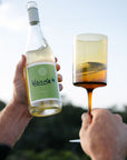 Person holding a bottle and glass of organic white wine with 'Verde' label against a blurred natural background
