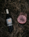 Blind Corner Organic Margaret River Cabernet bottle with a label on a dark, dried-grass surface next to a freshly poured glass of wine