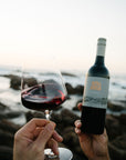 Person holding a bottle and glass of Blind Corner Organic and Biodynamic Margaret River Cabernet wine by the ocean