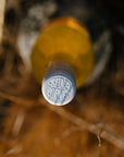 Blind Corner Organic and Biodynamic Margaret River Orange* in Colour Skin Contact Blend seen from directly above. The cap is embossed with the Blind Corner logo, the back ground is blurred, dry grass
