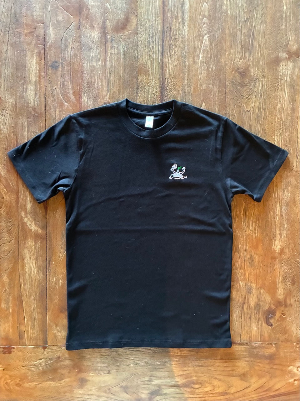 Black t-shirt with a small white Bar Nature logo on a wooden surface