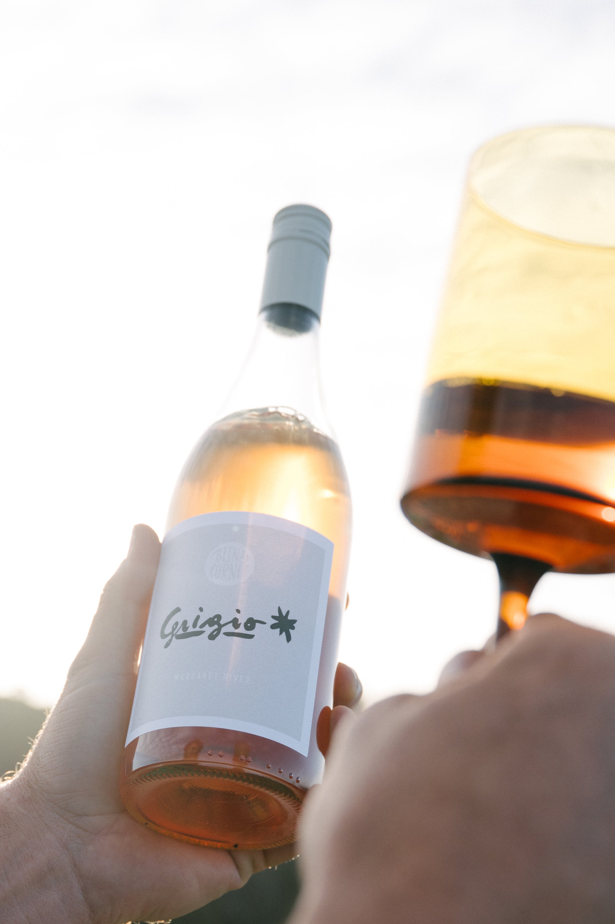 Person holding a bottle of Blind Corner Organic Biodynamic Pinot Grigio wine with a glass being filled.