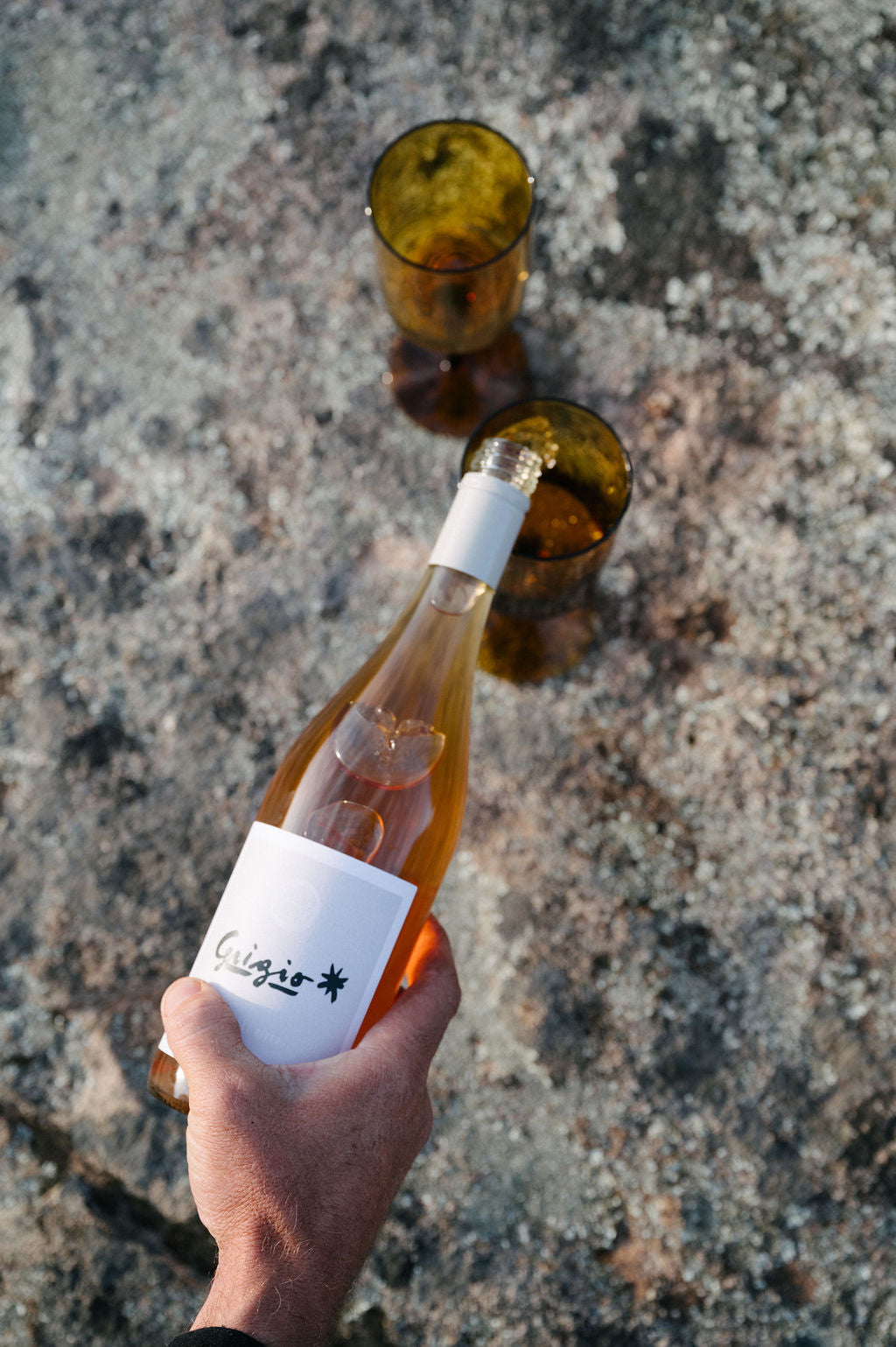 Hand pouring a bottle of Blind Corner's organic pinot grigio wine into an empty glass on a stony surface