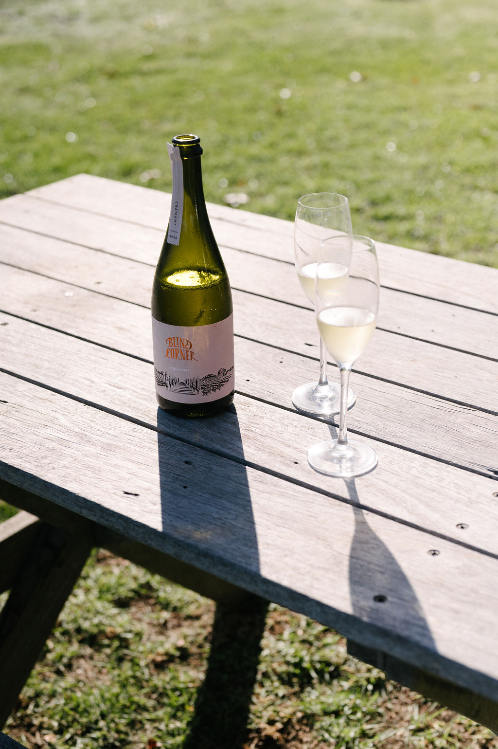 Bottle of Blind Corner Organic and Biodynamic Margaret River Cremant and two freshly poured glasses on a wooden table outdoors