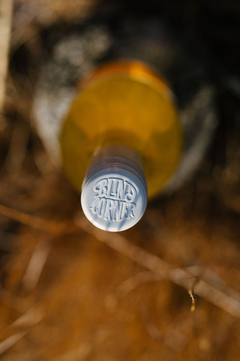 Blind Corner Organic and Biodynamic Margaret River Orange* in Colour Skin Contact Blend seen from directly above. The cap is embossed with the Blind Corner logo, the back ground is blurred, dry grass