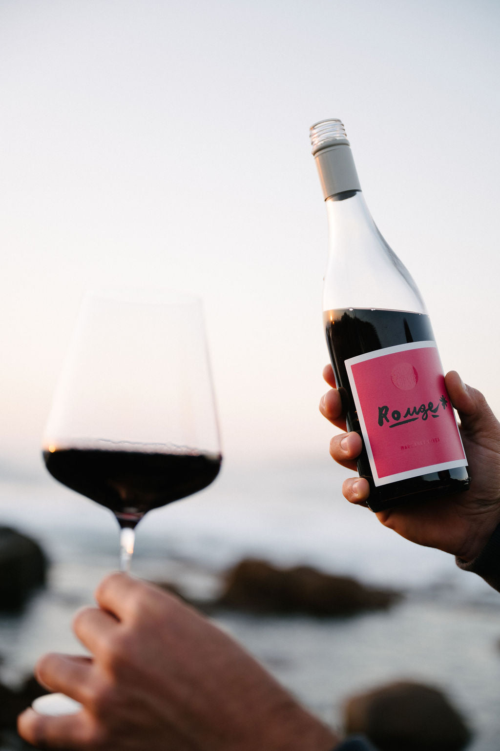 Person holding a bottle and glass of Blind Corner Organic and Biodynamic Margaret River Rouge by the sea