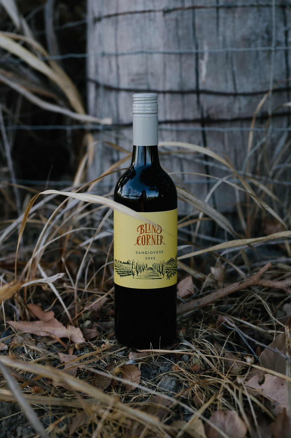 Blind Corner Organic and Biodynamic Margaret River Sangiovese bottle in front of a fence post and tall grass.