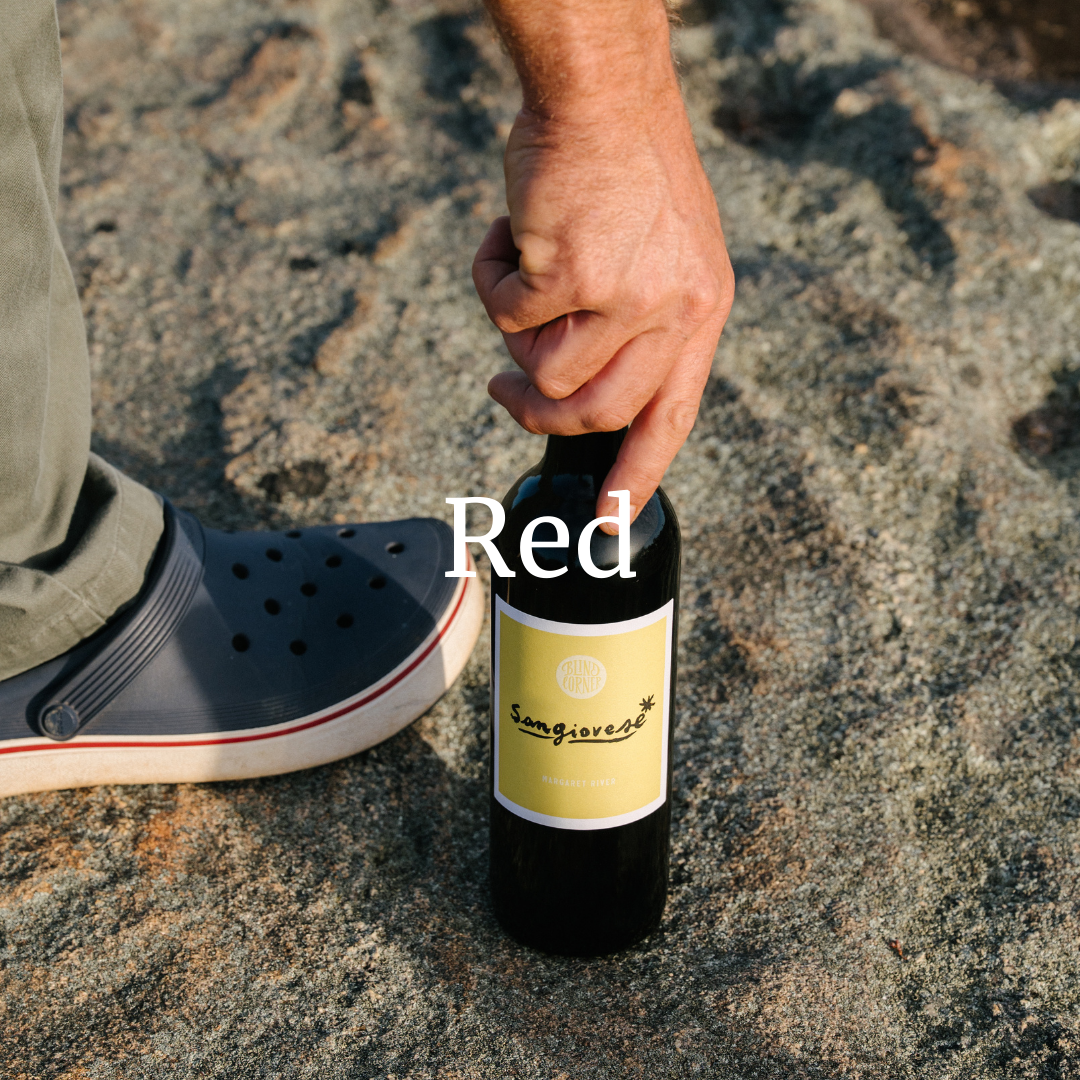 Person holding a bottle labeled 'Red' on a rocky surface