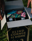 Open wine club box containing colourful cards and bottles of organic wine with 'Blind Corner is Home' text on the side.