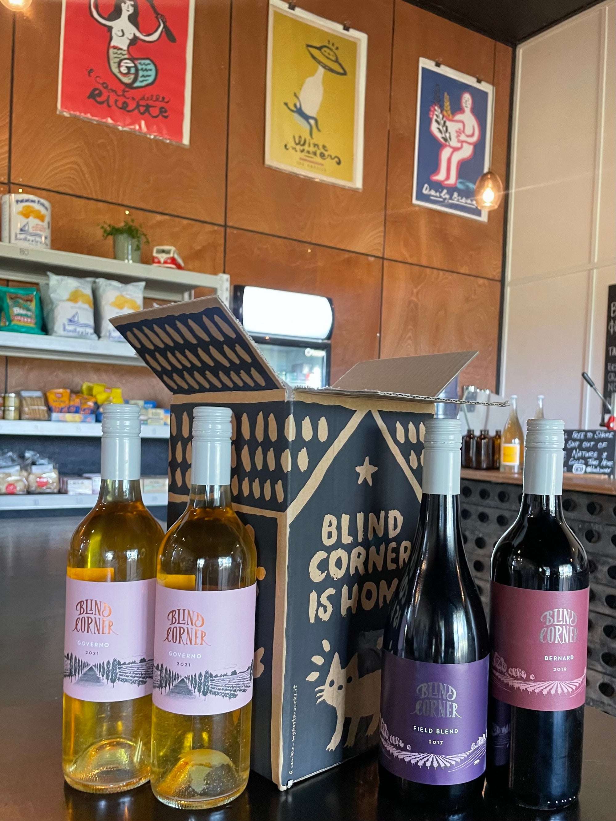 Blind Corner Wine Club Museum Release Box four wines on a table with bright colourful posters in the background
